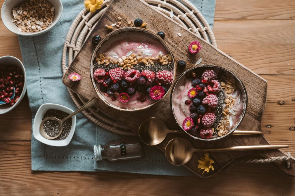 Draufsicht auf Beeren-Smoothie-Bowls mit Müsli auf einem rustikalen Holzbrett, perfektes veganes Frühstück.