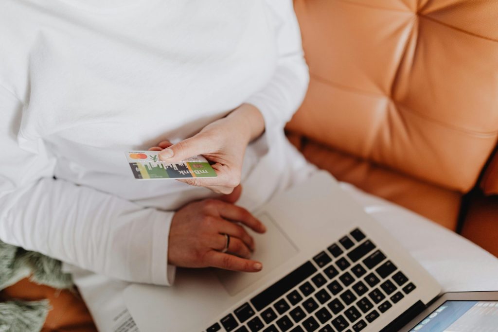 Eine Frau nutzt eine Debitkarte zum Online-Shopping auf einem Laptop im Haus.