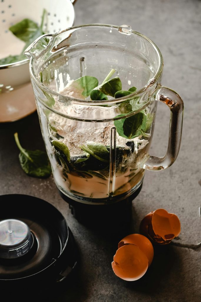 Ein Mixbecher aus Glas, gefüllt mit frischem Spinat und anderen Zutaten, bereit zum Mixen zu einem Smoothie.