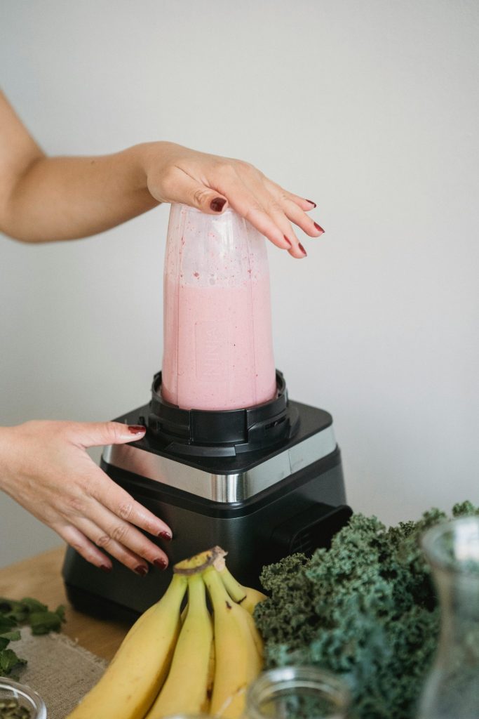 Hände machen mit einem Mixer einen nahrhaften rosa Smoothie mit Bananen und Grünkohl.
